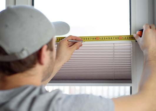 Man installing gray pleated blinds on the window